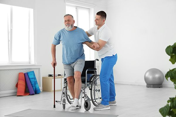 A rehabilitation professional helps a man with a cane into his wheelchair
